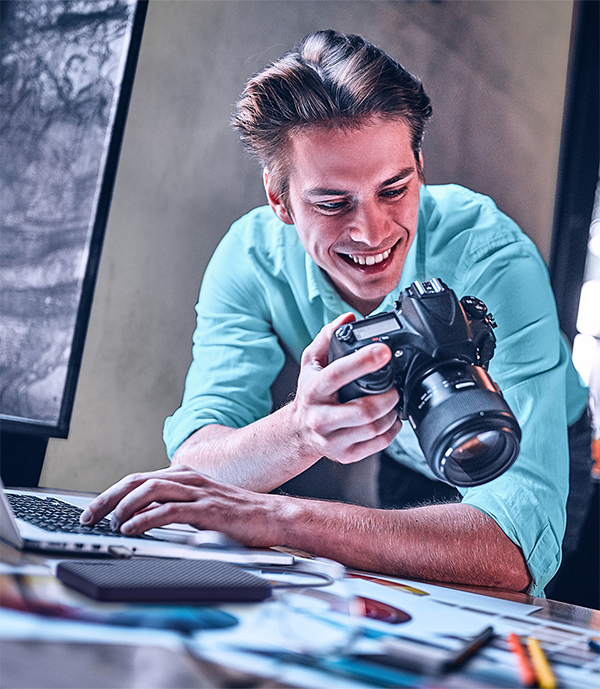 Hombre joven utilizando el Disco duro externo Toshiba Canvio Advance para traspasar archivos de c&aacute;mara profesional a notebook