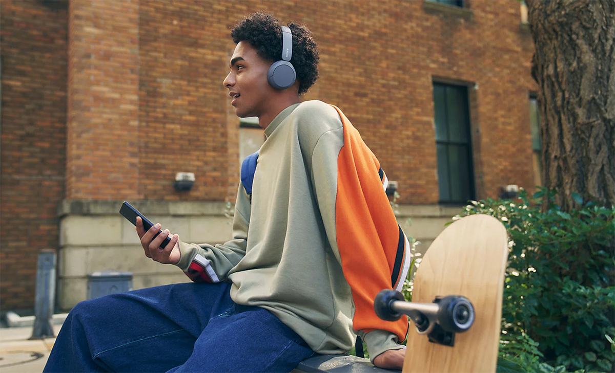 Hombre joven afroamericano utilizando los aud&iacute;fonos Sony WH-CH520 en un parque para realizar una llamada