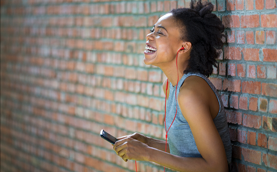 Mujer joven de color utilizando los aud&iacute;fonos JBL T310 USB-C en color rojo conectados a smartphone