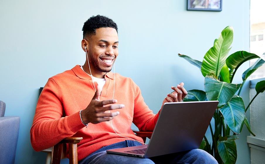 Hombre joven de color sentado con notebook en su regazo y utilizando JBL T310 USB-C color blanco para realizar videollamada