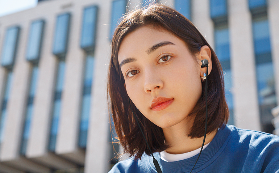 Plano detalle de mujer joven trigue&ntilde;a utilizando los JBL T310 USB-C color negro en un entorno exterior urbano