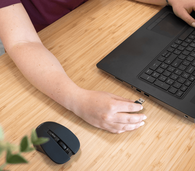 Vista detalle de mano femenina instalando Adaptador Bluetooth Trust Myna 5.4 en un notebook sobre un escritorio
