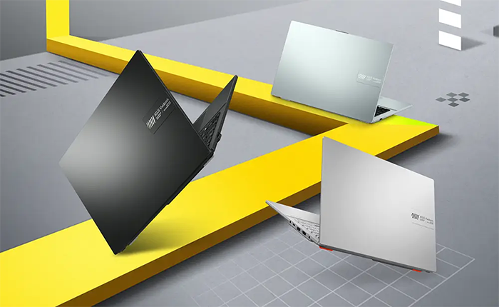 Vista frontal en &aacute;ngulo del notebook ASUS Vivobook Go 15 abierto. Muestra una pantalla de bordes delgados (NanoEdge) con un fondo de pantalla colorido y abstracto, un teclado completo con teclado num&eacute;rico y un touchpad amplio. El chasis es de color gris oscuro mate.