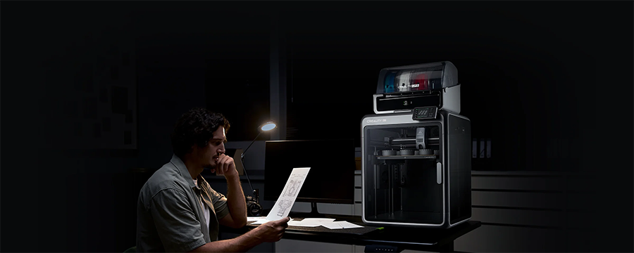 Hombre leyendo paper mientras impresora Creality K2 trabaja