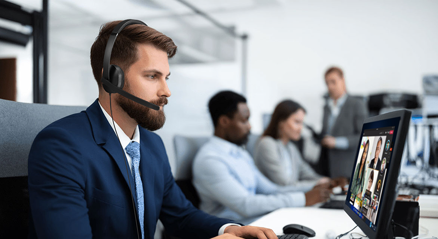 Hombre joven con barba sentado frente a un escritorio en una oficina usando los aud&iacute;fonos Lenovo Wired VoIP Headset con micr&oacute;fono con su ntoebook