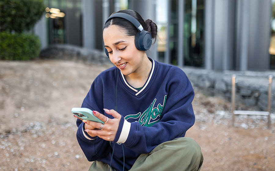 Mujer joven con el cabello recogido en exterior utilizando los aud&iacute;fonos JBL Tune 520 conectados a su smartphone